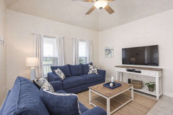 A living room with a sofa set, a coffee table, a TV, and a ceiling fan. - * EZ to Beach Sleeps Many * Very Clean * Pool (South Padre Island)