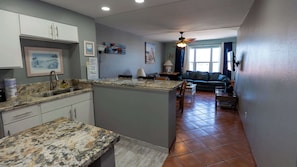 A kitchen with granite countertops, a dining area with a sofa, and a window with curtains.