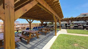Un patio techado al aire libre con mesas y sillas de picnic, una cerca de madera y una zona de césped.