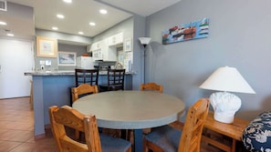 A dining area with a round table, wooden chairs, a lamp, and a painting on the wall.