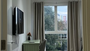 A bedroom with a bed, a desk, a chair, a TV, and a window with curtains.