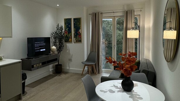 A modern living room with a dining area, a flat-screen TV, and a large window with curtains.