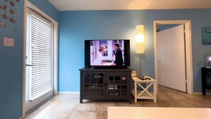 Uma sala de estar com televisão, abajur e uma porta.