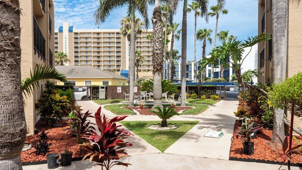 A hotel courtyard with palm trees, a central fountain, and a pathway leading to the building entrance. - Near Beach " Updated " Pool & Hot Tub (South Padre Island)