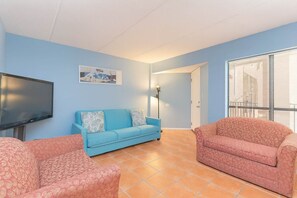 A living room with a flat-screen TV, a blue sofa, a pink sofa, and a patterned armchair.