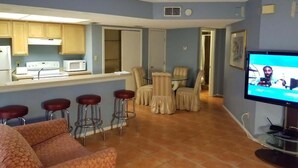 A living room with a kitchen area, a television, and a bar with stools. - * Heart of Entertainment District (South Padre Island)