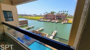A view from a balcony overlooking a marina with boats, a pool, and a building with a pool area. - Channel Front with Pool " Hot Tub " Patio (South Padre Island)