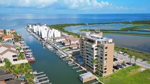 A marina with docked boats, a large building with multiple floors, and a view of the ocean and wetlands. - Channel Front with Pool " Hot Tub " Patio (South Padre Island)
