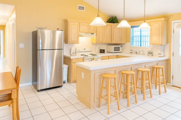 A modern kitchen with a stainless steel refrigerator, wooden cabinets, a white countertop, and bar stools.