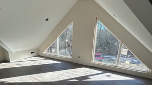 A spacious attic room with high ceilings, large windows, and a sloped roof.