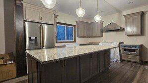 A kitchen with dark cabinets, a stainless steel refrigerator, a large island, and pendant lighting.