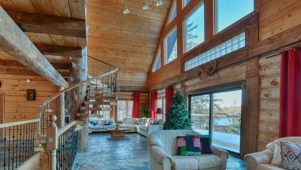 L’intérieur d’une cabane en rondins, avec un escalier, des murs en bois, une grande fenêtre et un sapin de Noël.