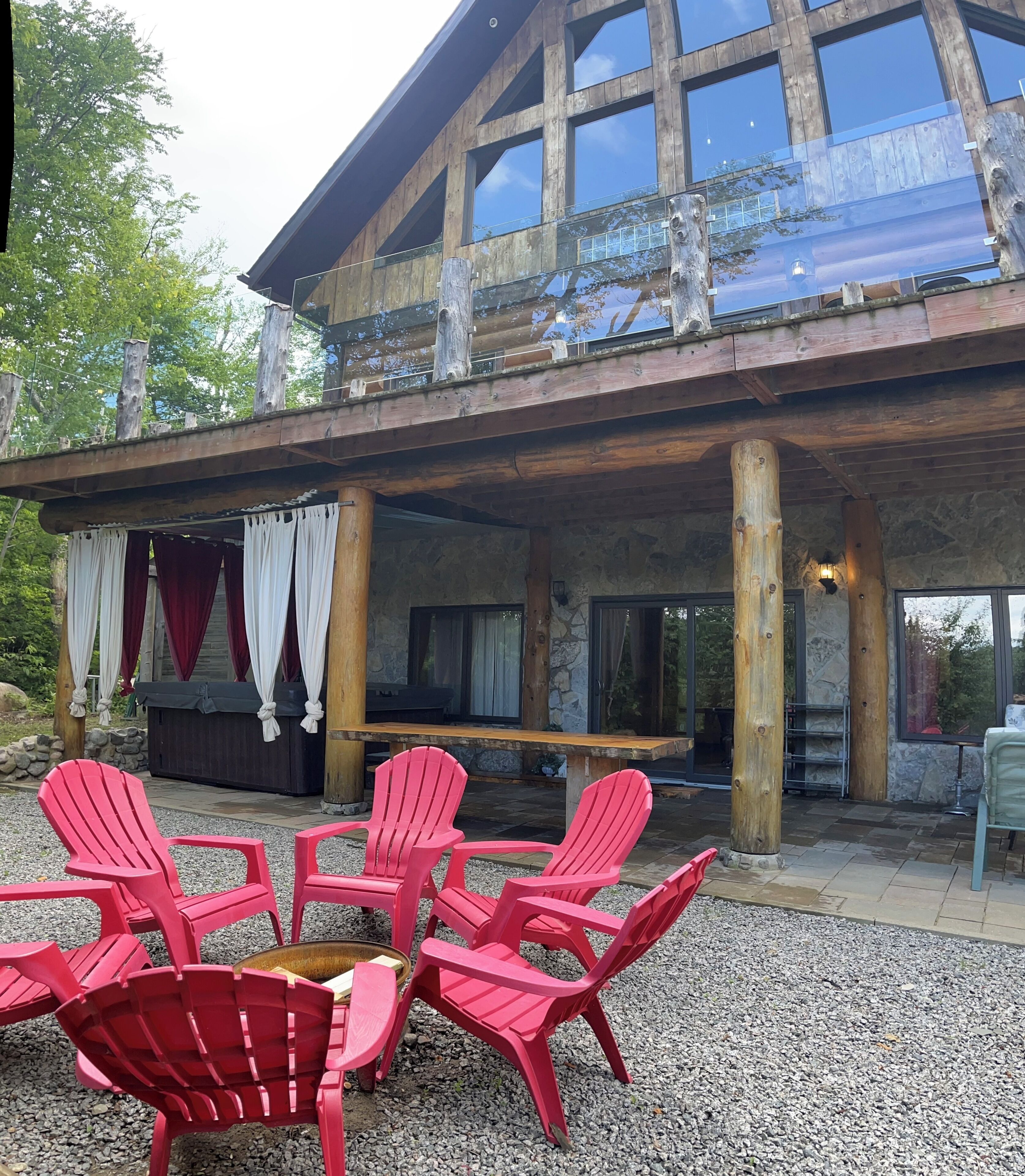 Un edificio in legno con un patio coperto, dotato di poltrone Adirondack rosse e un camino in pietra.