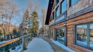 Une cabane en rondins avec une terrasse enneigée et de grandes fenêtres.