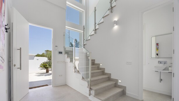 A modern staircase with glass railings leading to a bathroom with a white sink and mirror. - Villa 'Habana' with Lake View, Wi-Fi and Air Conditioning (Poblado de Sancti Petri)
