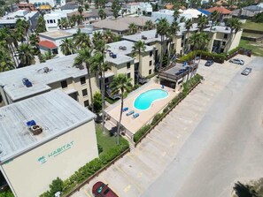A residential building with a swimming pool, parking area, and several palm trees. - * Pool  * 2 Levels * 2 Patios * Near Beach (South Padre Island)