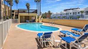 A swimming pool with lounge chairs, a small deck area, and a building with balconies in the background. - * Pool  * 2 Levels * 2 Patios * Near Beach (South Padre Island)