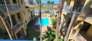 A multi-story building with balconies, a swimming pool, and palm trees.