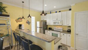 A kitchen with white cabinets, a stainless steel refrigerator, a microwave, and a stove. There are two bar stools and a trash can. - * Patio to Pool * Walk to Beach * Fresh Like New (South Padre Island)