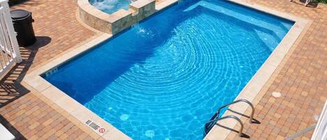 A rectangular swimming pool with a hot tub, surrounded by a tiled deck and white lounge chairs.