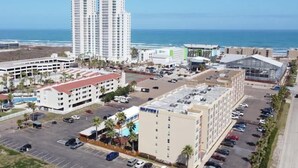 A hotel with a parking lot, a pool area, and a view of the ocean.