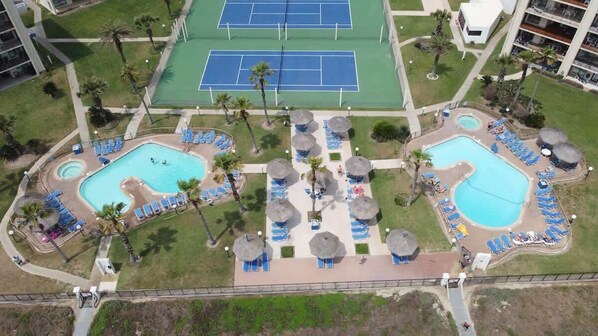 An aerial view of a resort with multiple swimming pools, tennis courts, and sun loungers.