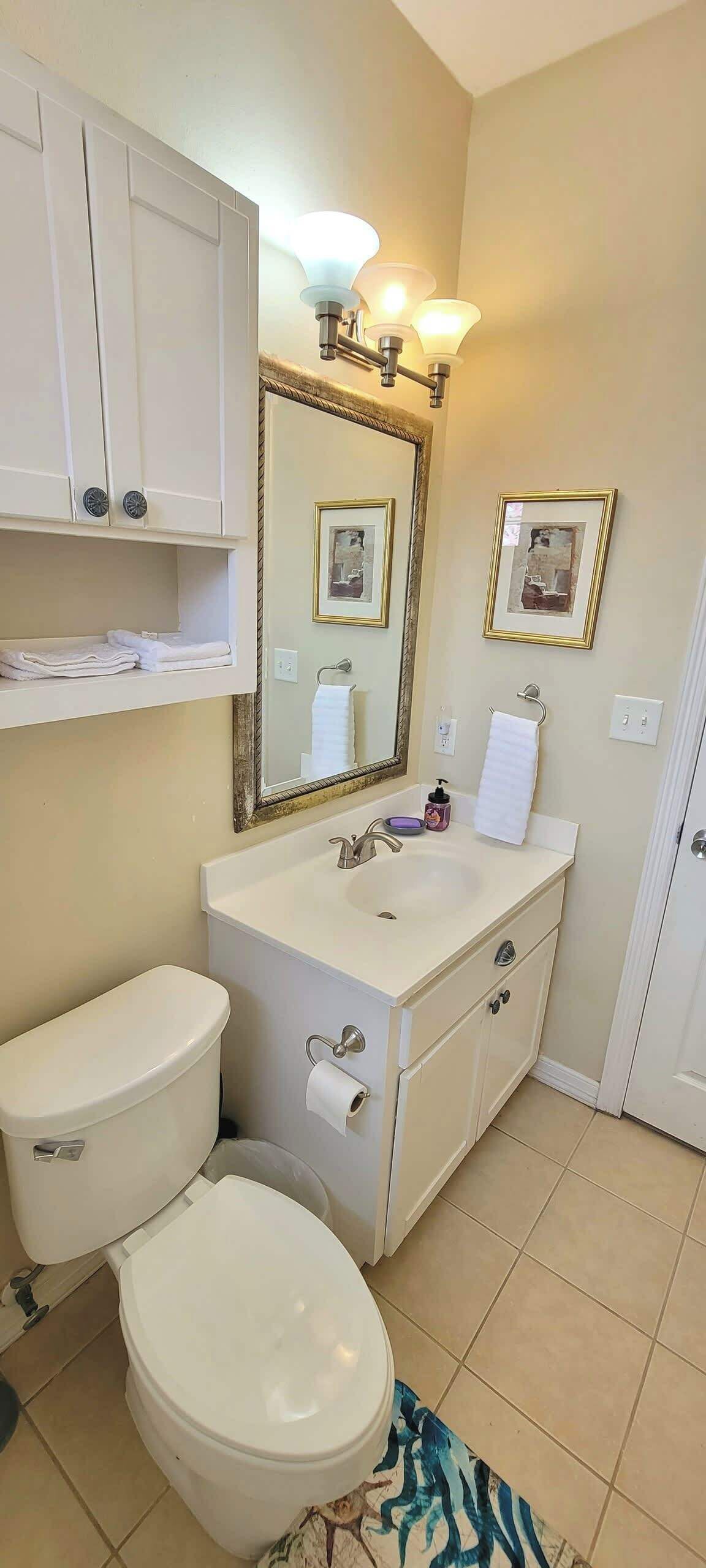 A bathroom with a toilet, sink, vanity, and a mirror.