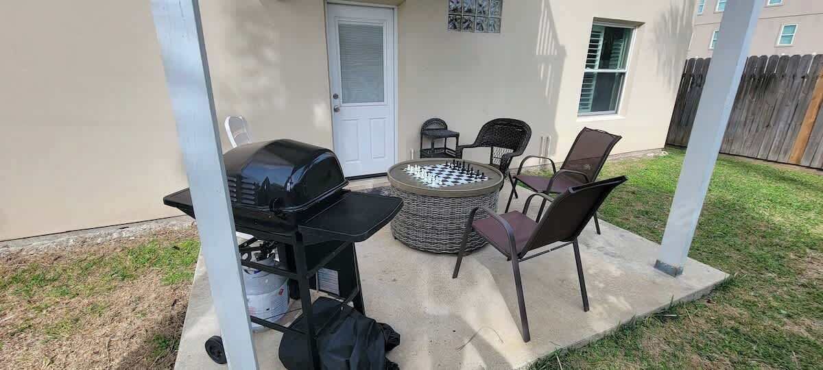 Een terras buiten met een barbecue, een ronde tafel en vier stoelen.