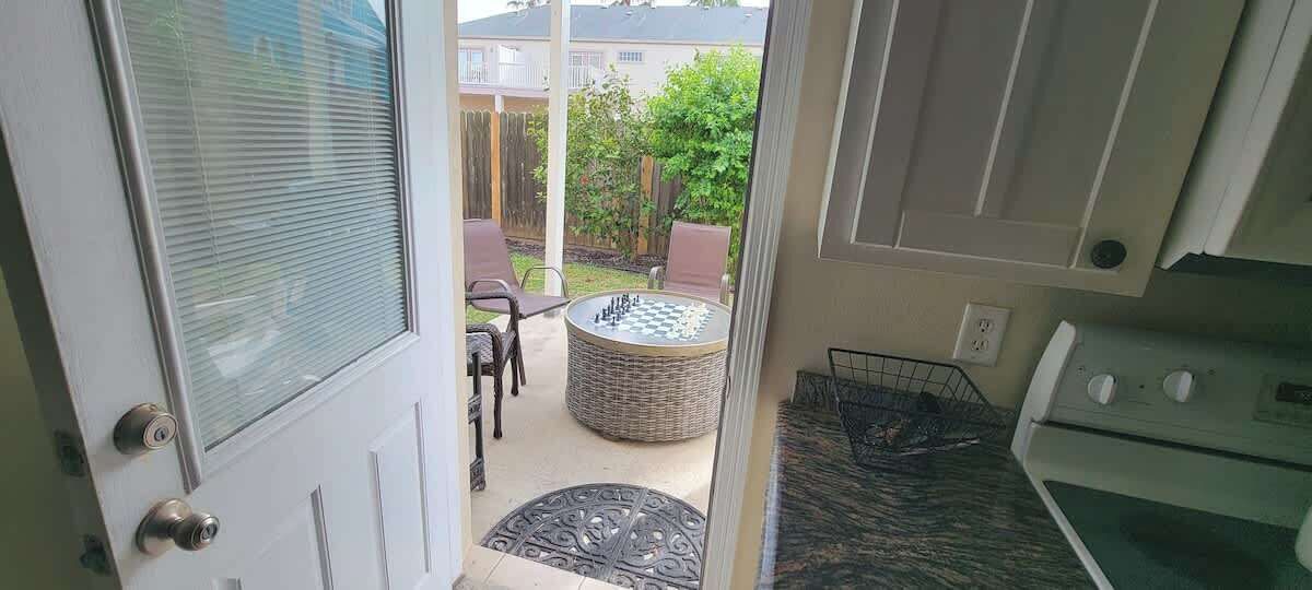 A view from a door into a room with a wicker table, chairs, and a small garden area visible through the window.