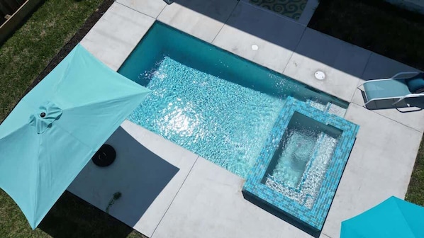 Une piscine rectangulaire avec un petit jacuzzi, entourée d’une terrasse en béton.
