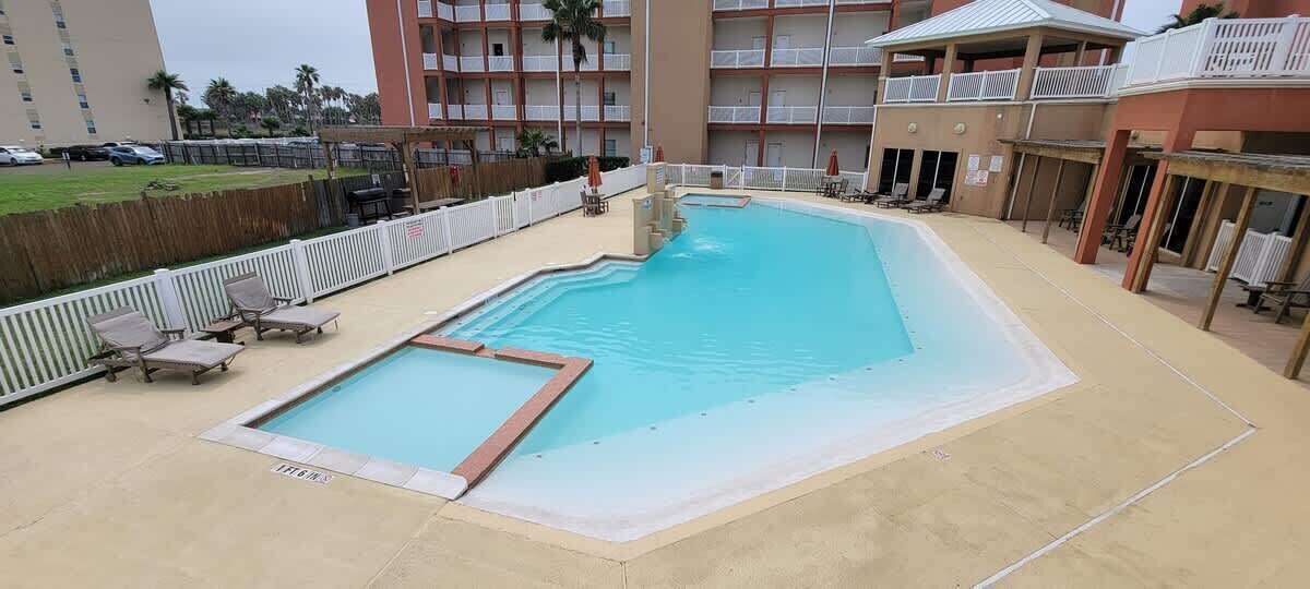 Una piscina con un pequeño jacuzzi, sillas de descanso y una terraza de madera.