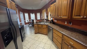 A kitchen with wooden cabinets, a stainless steel refrigerator, a sink, and a dining area with a table and chairs.
