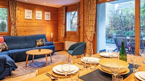 A cozy wooden cabin interior with a sofa, dining table set for four, and a view of the outdoors. - Alpine Garden - Truly hidden gem with sunny garden in Chamonix town center (Chamonix-Mont-Blanc)