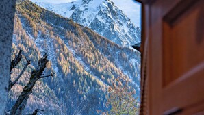 A view of a mountainous landscape through a window with wooden furniture. - Alpine Garden - Truly hidden gem with sunny garden in Chamonix town center (Chamonix-Mont-Blanc)