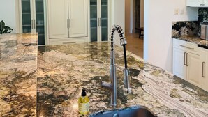 Eine Küche mit Granit-Arbeitsplatte, Edelstahl-Spüle und weißen Schränken.