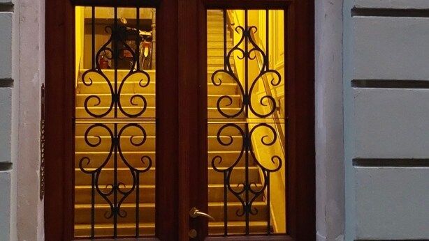 A double wooden door with intricate ironwork, a small window above it, and a house number plaque on the wall.