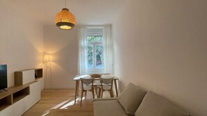 A modern living room with a sofa, a dining table with chairs, a TV, and a lamp.
