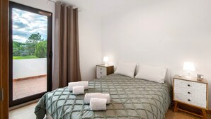 A bedroom with a bed, two bedside tables, a nightstand, a sliding glass door to a balcony, and a view of greenery. - Holiday Home 'Cool Motion 2149' with Private Terrace, Wi-Fi and Air Conditioning (Albufeira)