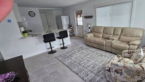 A modern living room with a beige sofa, a coffee table, and a dining area with a kitchen counter. - Downtown Getaway Casita (Bradenton)