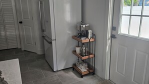 A kitchen with a built-in refrigerator, a coffee machine on a wooden cart, and a window with a view of a white fence. - Downtown Getaway Casita (Bradenton)
