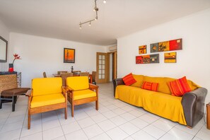 Ein Wohnzimmer mit einem gelben Sofa, zwei gelben Sesseln, einem Esstisch mit Stühlen und Kunstwerken an den Wänden.