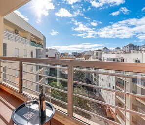 A balcony with a glass table, a bottle, and a glass, overlooking a cityscape with buildings and a clear sky. - Apartment 'Cool Motion Rocha Beach T1' with Balcony, Wi-Fi and Air Conditioning (Portimão)