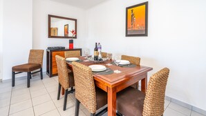 A dining area with a wooden table set for six, surrounded by wicker chairs, a mirror, and a framed artwork on the wall. - Apartment 'Cool Motion Rocha Beach T1' with Balcony, Wi-Fi and Air Conditioning (Portimão)