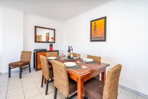 Un comedor con una mesa de madera dispuesta para seis personas, rodeada de sillas de mimbre, un espejo y una obra de arte enmarcada en la pared.