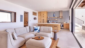 Un salon moderne avec un canapé d’angle, une table basse et un coin cuisine doté de meubles en bois et d’un dosseret carrelé.