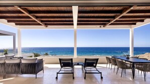 Un espace extérieur moderne aménagé avec des sièges, offrant une vue sur l’océan, comprenant une table, des chaises et une pergola au-dessus.