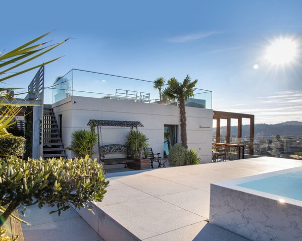 A modern outdoor pool area with a glass balustrade, a palm tree, and a view of the cityscape.