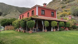 A red villa with a tiled roof, surrounded by a well-maintained lawn and potted plants. - Beautiful garden, spectacular view and privacy, ideal for nature lovers. (Tegueste)