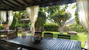 An outdoor patio area with a wooden table and chairs, surrounded by greenery and a view of a mountainous landscape. - Beautiful garden, spectacular view and privacy, ideal for nature lovers. (Tegueste)
