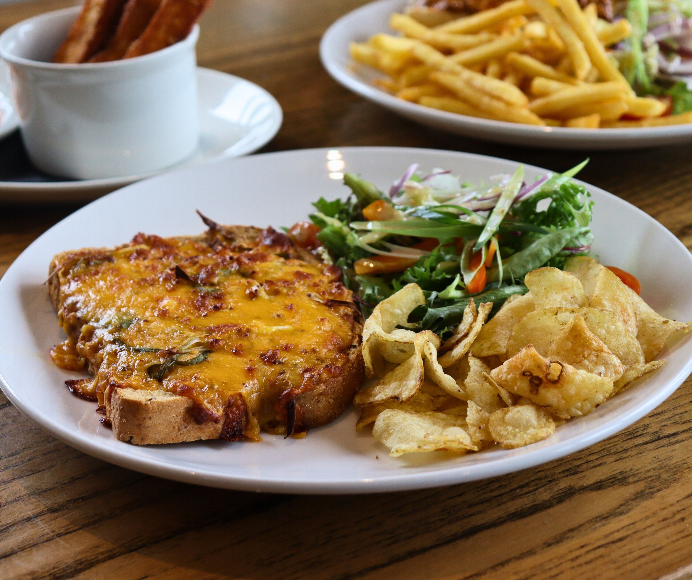 Ein Teller mit einem Steak, überzogen mit geschmolzenem Käse, dazu ein gemischter Salat und Kartoffelchips.